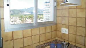 A bathroom with a window view of a cityscape, a sink, and a countertop with two blue mugs. - Family apartment, sea view, pets welcome - 6 guests (Gandia)