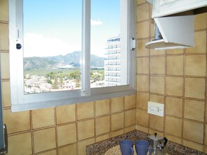 Ein Badezimmer mit Fensterblick auf eine Stadtlandschaft, einem Waschbecken und einer Ablage mit zwei blauen Tassen.