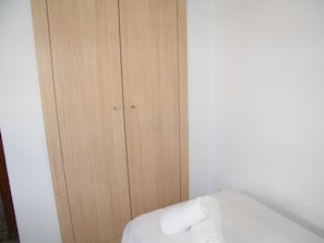 Ein Zimmer mit einem Holzschrank und einem Bett, auf dem ein gerolltes weißes Handtuch liegt.