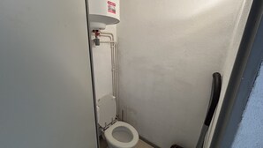 Um banheiro pequeno e estreito, com vaso sanitário, secador de mãos e um cano aparente.