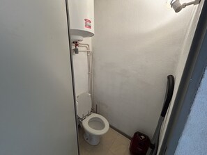 Ein kleines, schmales Badezimmer mit Toilette, einem Händetrockner und freiliegenden Rohren.