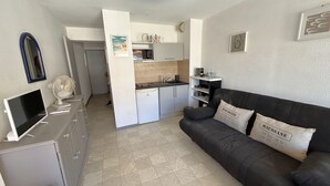 Um espaço compacto com cozinha compacta, sofá preto com almofadas, televisão de tela plana e um refrigerador pequeno.