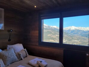 A room with a bed, pillows, a wall-mounted lamp, and a window with a mountain view. - Prestige chalet mountain views - 14 guests (Pra-Loup)