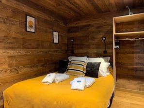 Ein Zimmer mit Holzwänden, einem Bett, zwei Wandleuchten und einem gerahmten Bild.