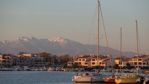 Ein Yachthafen mit mehreren Segelbooten, Gebäude im Hintergrund und einer Bergkette in der Ferne.