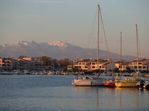 A marina with several sailboats docked, buildings in the background, and a mountain range in the distance. - Practical apartment with terrace - 6 guests (Saint-Cyprien)