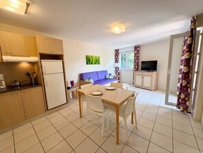 A compact kitchen with a refrigerator, stove, and dining area with chairs and a table. - Practical apartment with terrace - 6 guests (Saint-Cyprien)