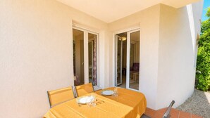 Eine Terrasse mit Tisch für zwei Personen, eine Glastür und Blick auf einen Garten.