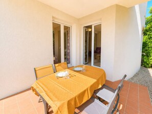 A patio with a table set for two, a sliding glass door, and a view of a garden. - Practical apartment with terrace - 6 guests (Saint-Cyprien)