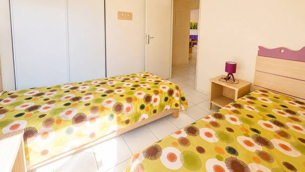 Ein Zimmer mit zwei Betten, einem Holfnachtkästchen, einer Tür und Blick in ein weiteres Zimmer.