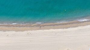 Eine Vogelperspektive zeigt einen Strand mit klarem türkisblauem Wasser, einem Sandufer und einer Person, die am Strand entlanggeht.