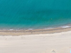 An aerial view of a beach with clear turquoise water, a sandy shore, and a person walking along the beach. - Practical apartment with terrace - 6 guests (Saint-Cyprien)