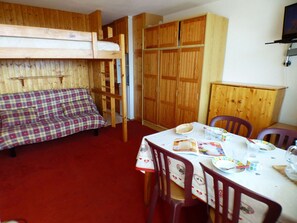 A room with a bunk bed, a dining table with chairs, and wooden cabinets. - Charming studio, mountain view - 3 guests (Les Saisies)