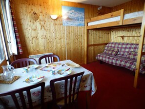 A cozy room with a bunk bed, a dining table set with plates, cups, and a pitcher, and a window with curtains. - Charming studio, mountain view - 3 guests (Les Saisies)