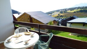 En balkon med et bord og stole, der kigger ud over et landligt landskab med huse og bjerge.