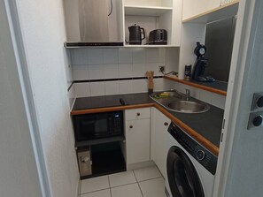 Eine kleine Küche mit Mikrowelle, Backofen, Spüle und Waschmaschine.