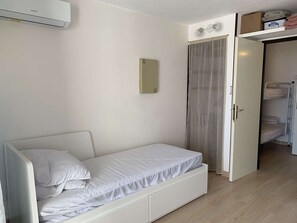 A single-bed room with a white bed, a small bedside table, a mirror, a wardrobe, and a ceiling fan. - Studio cabin sea view, pets and parking - 4 guests (Fleury-Saint-Pierre-la-Mer)