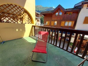 A balcony with a red chair, a wooden fence, and a view of mountain buildings. - Cozy apartment in Valmorel center - 4 guests (Valmorel)