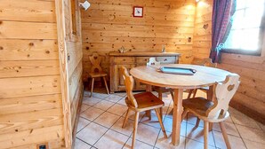 Ein Holzinnenraum mit einem runden Tisch, Stühlen, einer kleinen Küchenzeile und einem Fenster mit Vorhängen.