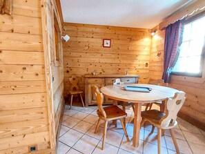 Ein Holzinnenraum mit einem runden Tisch, Stühlen, einer kleinen Küchenzeile und einem Fenster mit Vorhängen.