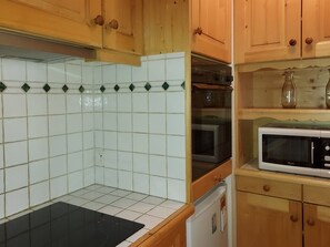 Eine Küche mit Holzausstattung, einer Mikrowelle, einem Backofen und einer schwarzen Arbeitsplatte.