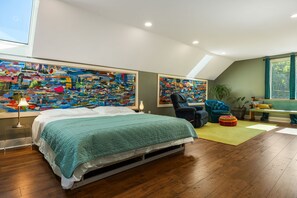 Une chambre à coucher comprenant un lit, une chaise, un canapé et deux grands tableaux abstraits.