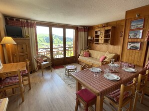 A cozy room with a wooden floor, a sofa, a dining table set with plates and glasses, and a television on a cabinet.
