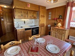 A kitchen with wooden cabinets, a dishwasher, and a table set for two with plates and glasses. - Cozy apartment, panoramic view - 6 guests (Les Saisies)