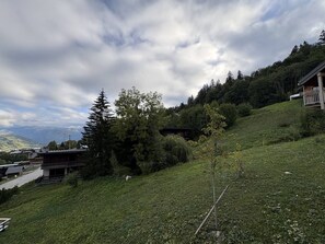 A hillside with a building, trees, and a view of distant mountains. - Cosy apartment with mountain view - 7 guests (Valmorel)