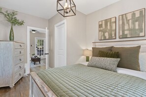 A bedroom with a bed, a dresser, a lamp, and two paintings on the wall.