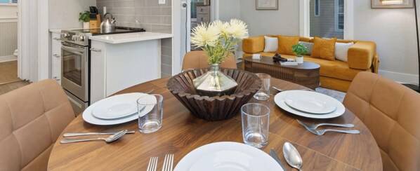 A dining table set with plates, cutlery, and glasses, surrounded by a brown table runner and a decorative vase. - Akin East | Pet-Friendly Furnished Monthly Rental (Fort Collins)