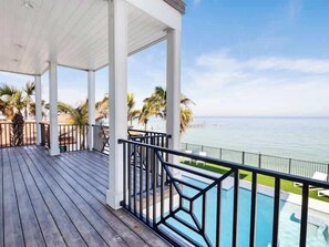 Una terraza de madera con piscina, una estructura blanca y vista al océano.