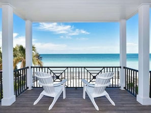 A covered outdoor area with two white chairs facing a beach.