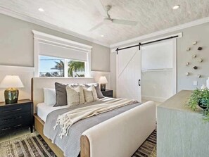 Un dormitorio con cama, mesitas de noche, ventana, ventilador de techo y puerta corredera.