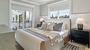 A bedroom with a large bed, two bedside tables, a ceiling fan, and a view through a sliding glass door.