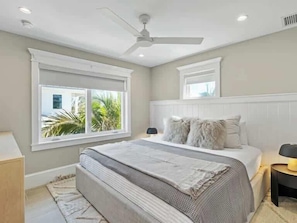 Une chambre à coucher avec un grand lit, un ventilateur de plafond, une fenêtre donnant sur un beau paysage et une table de chevet.