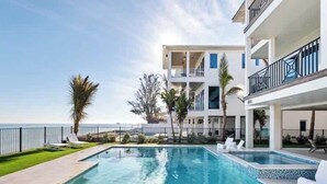 A modern hotel with a pool, white lounge chairs, and a view of the sea.