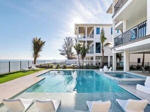 A modern hotel with a pool, white lounge chairs, and a view of the sea.