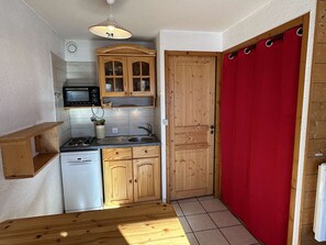 Ett kompakt kök med träskåp, en mikrovågsugn, ett handfat och en röd gardin.