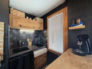 A compact kitchen with a built-in stove, a coffee maker, and a window with blinds. - Cozy apartment, mountain view - 5 guests (Valmorel)