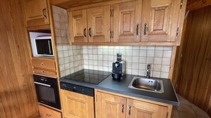 Uma cozinha compacta com armários de madeira, bancada preta, forno embutido e pia.
