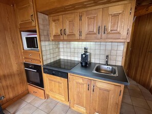 A compact kitchen with wooden cabinets, a black countertop, a built-in oven, and a sink. - Duplex panoramic mountain view - 8 guests (Les Saisies)