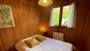 Um quarto com cama, mesa de cabeceira, luminária, radiador e janela com cortinas.