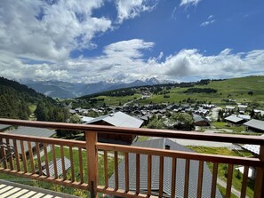 A residential area with houses, a wooden balcony railing, and a mountain range in the background.