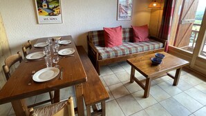 Uma sala de jantar com uma mesa de madeira posta para quatro pessoas, um sofá com almofadas xadrez e uma mesinha com uma tigela azul.