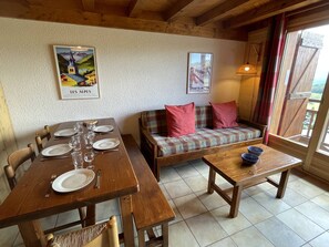 A dining area with a wooden table set for four, a sofa with plaid cushions, and a small table with a blue bowl. - Duplex panoramic mountain view - 8 guests (Les Saisies)