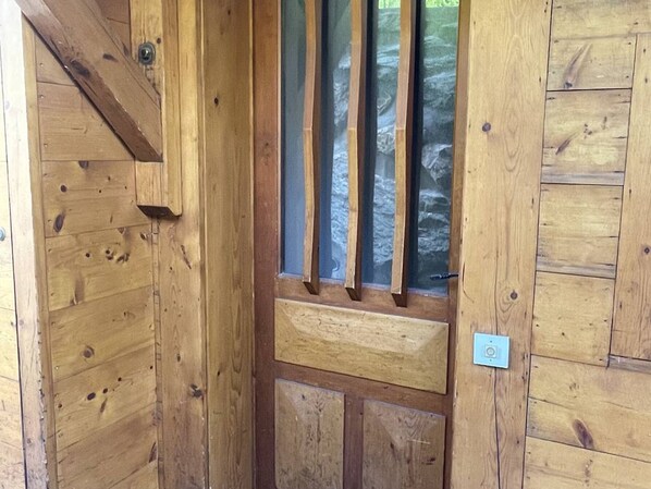 A wooden door with a vertical window, a metal handle, and a small light switch on the wall.