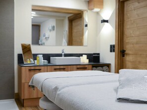 Ein modernes Badezimmer mit einem hölzernen Waschtisch, einem großen Spiegel und einem Bett mit einem weißen Handtuch.