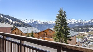A mountain lodge with a wooden facade, a balcony with a metal railing, and a view of snow-capped mountains. - Apartment with panoramic view - 6 guests (Les Saisies)