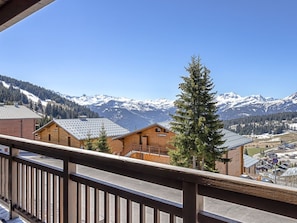 Eine Berglodge mit Holzfassade, einem Balkon mit Metallgeländer und Blick auf schneebedeckte Berge.